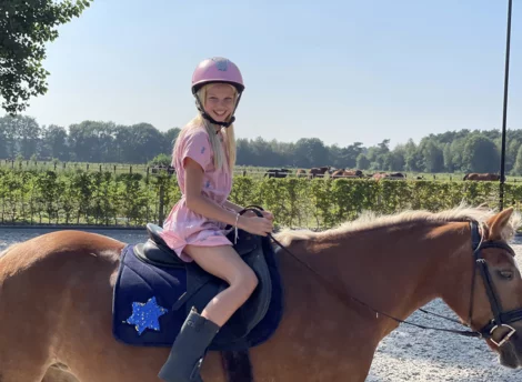 Meisje met roze tok zit trots op een paard